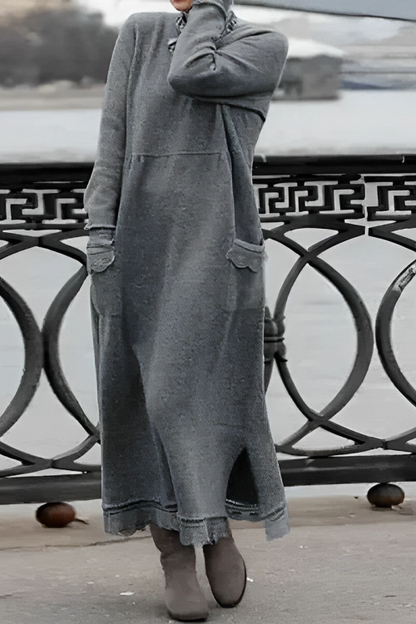 Person wearing a long gray sweater dress standing by a waterfront with a decorative metal railing.