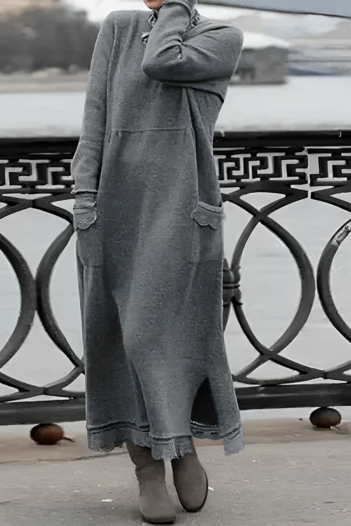 Person wearing a long gray sweater dress standing by a waterfront with a decorative metal railing.