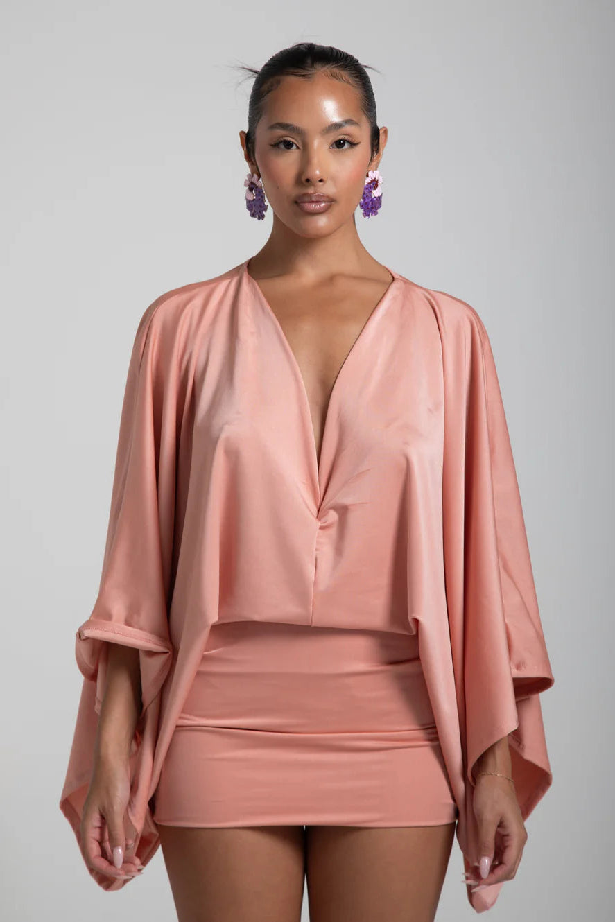 Woman wearing a pink outfit with a draped top and matching skirt against a gray background
