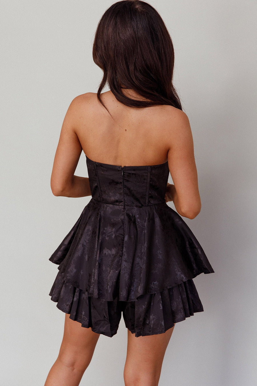 Woman wearing a black strapless dress with ruffled layers on a plain background