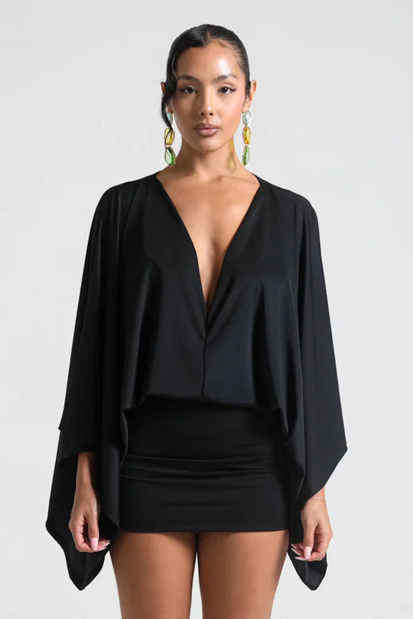 Woman wearing a black outfit with a cape on a white background