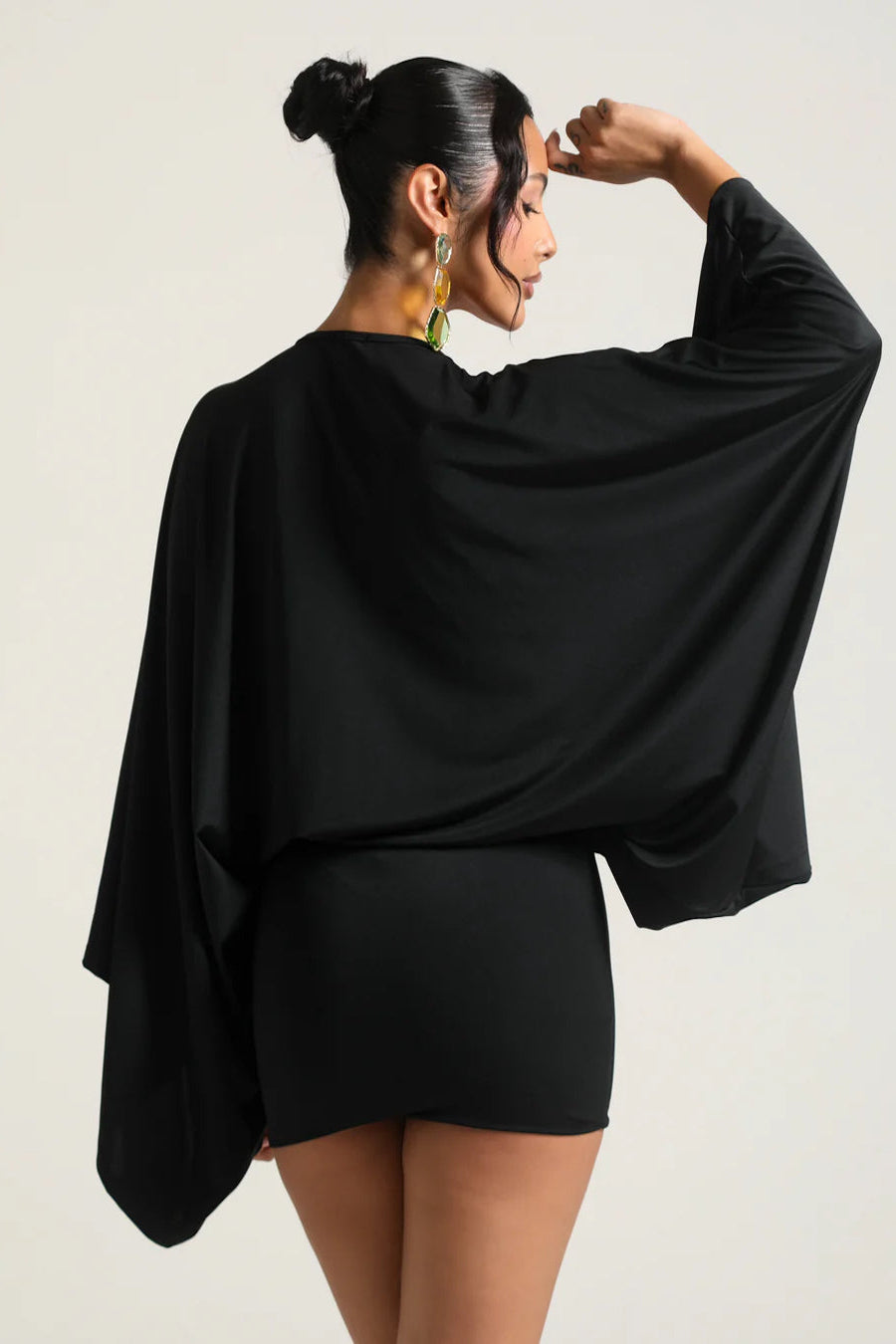 Woman wearing a black outfit with a cape-like garment on a plain background