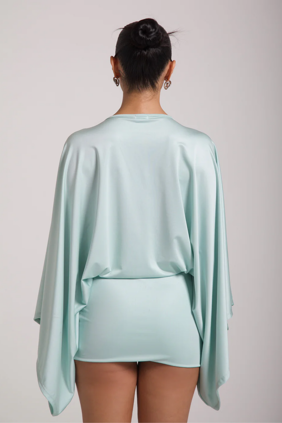 Person wearing a light blue outfit with a cape on a plain background