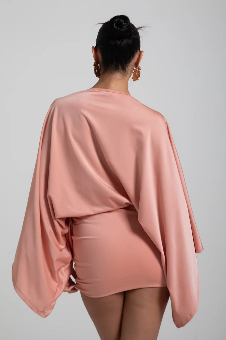 Person wearing a pink outfit with a draped top on a plain background