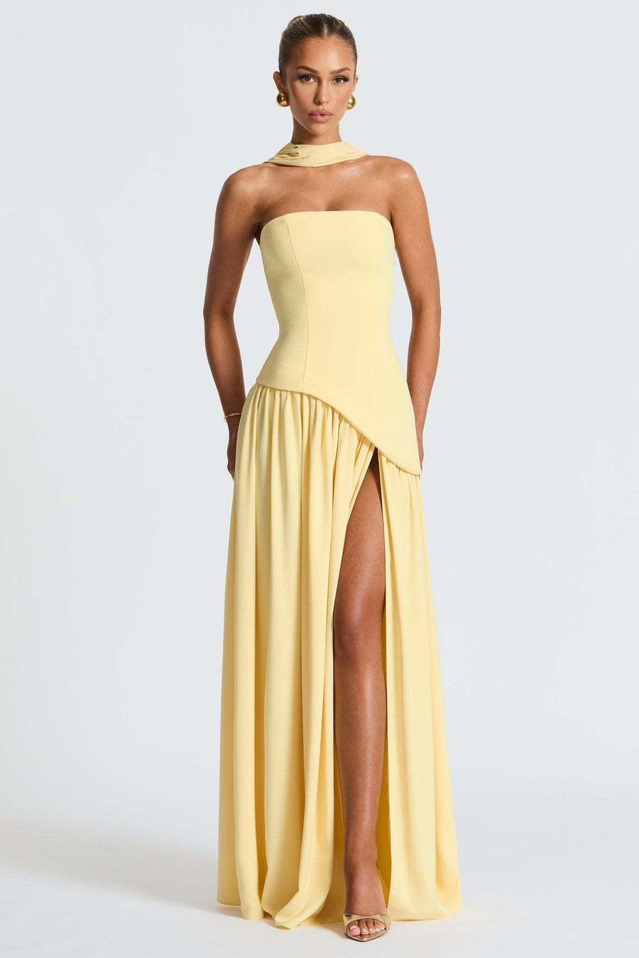 Woman wearing a yellow strapless gown with a slit on a light gray background