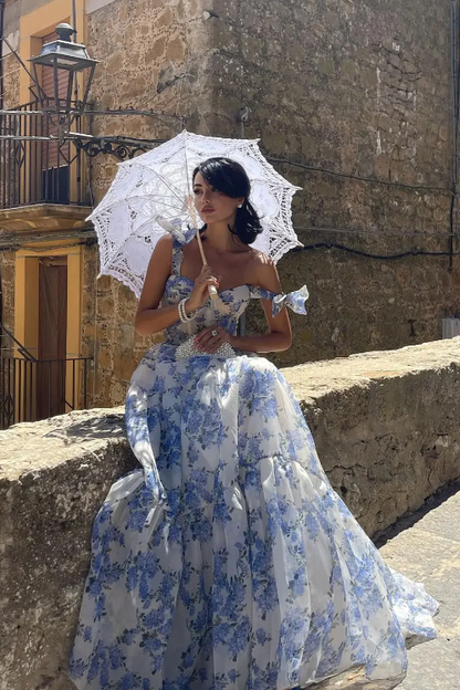 Woman in a blue floral dress holding a white parasol in an old stone street.
