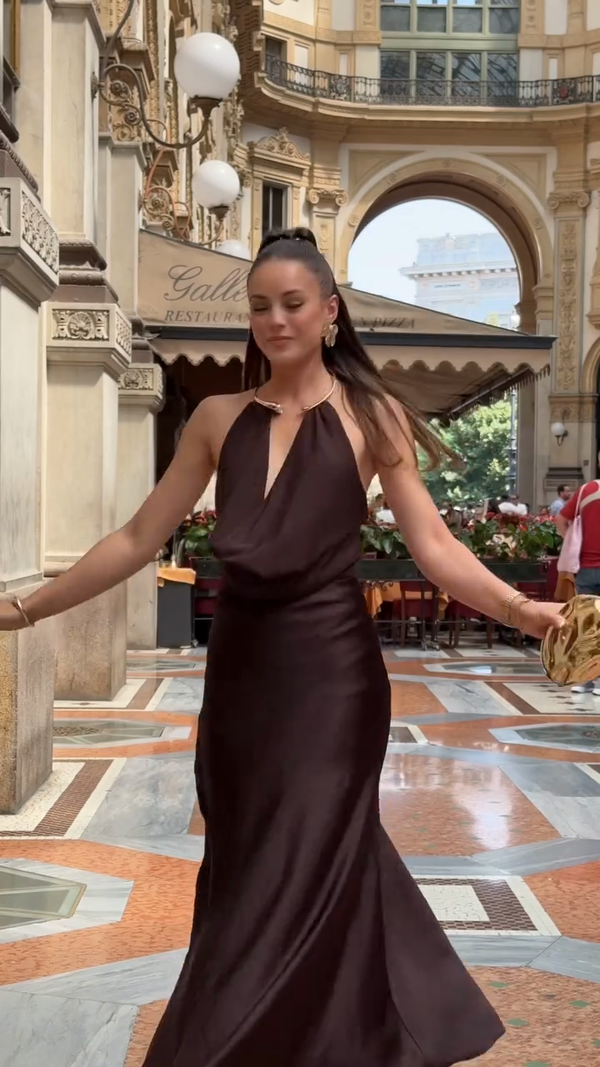 Woman in a dark brown evening gown standing in an elegant indoor setting with decorative floor and architecture.